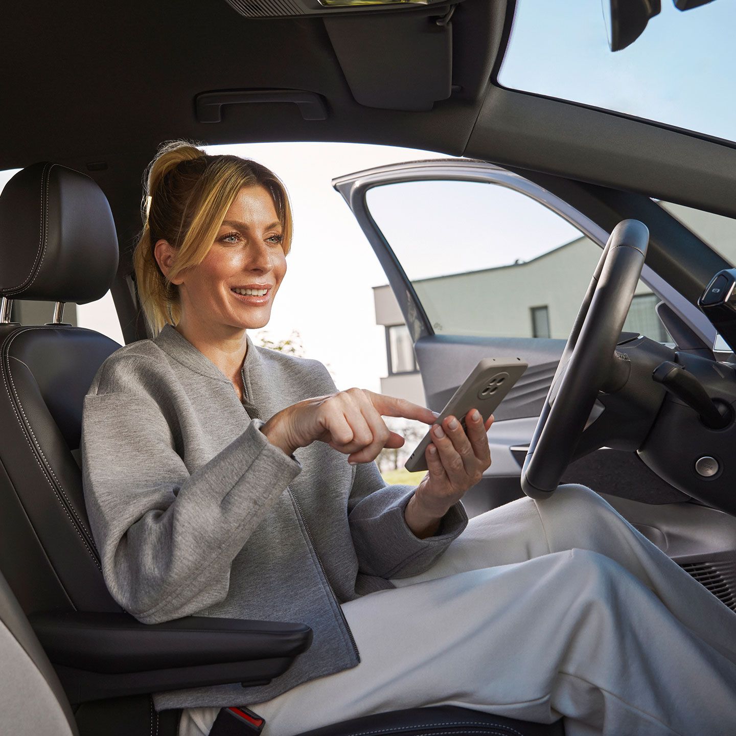 Eine Frau sitzt in einem Volkswagen auf dem Fahrersitz und bedient ein Smartphone. Der Innenraum des Autos wirkt hochwertig. 