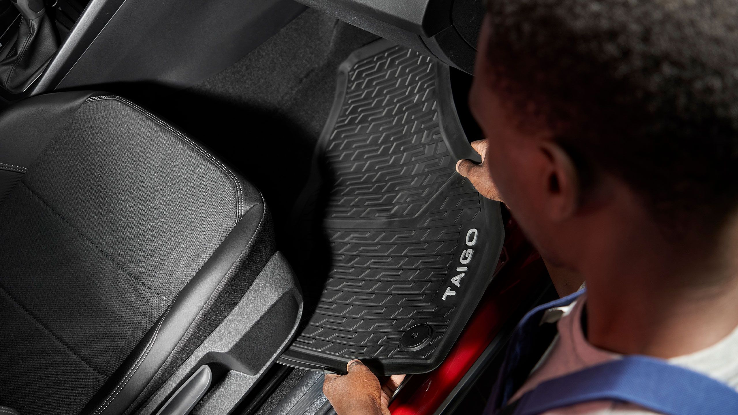 Ein Volkswagen Mitarbeiter legt eine Gummifußmatte mit Taigo Schriftzug in einen Volkswagen.