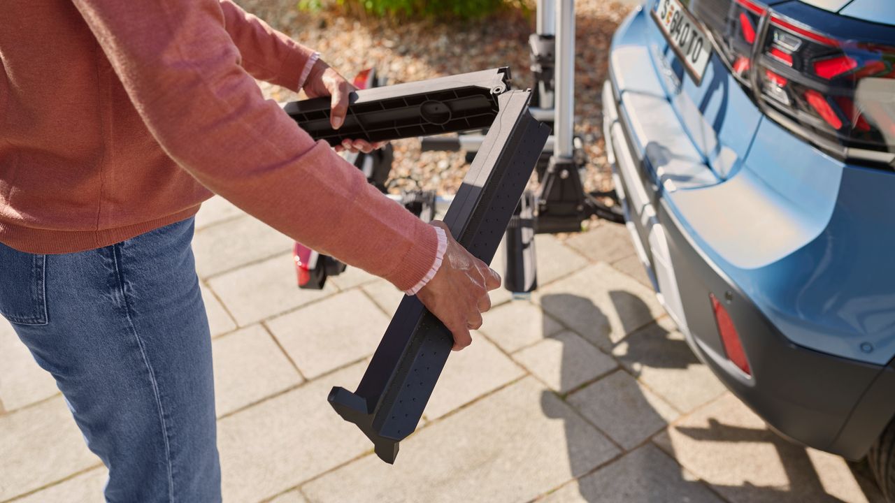 Eine Frau montiert eine Auffahrschiene am Heck eines blauen Volkswagen T-Cross