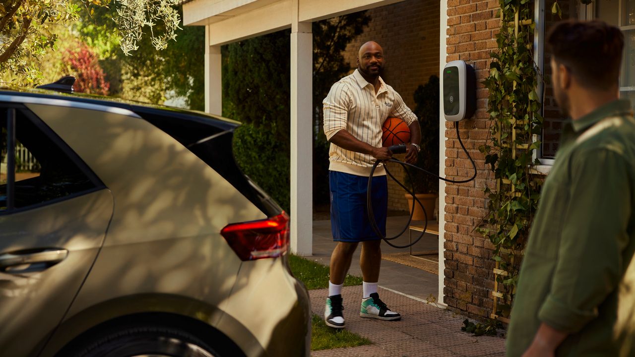 Muž se baví se sousedem a drží nabíjecí kabel wallboxu. V popředí stojí Volkswagen ID.3