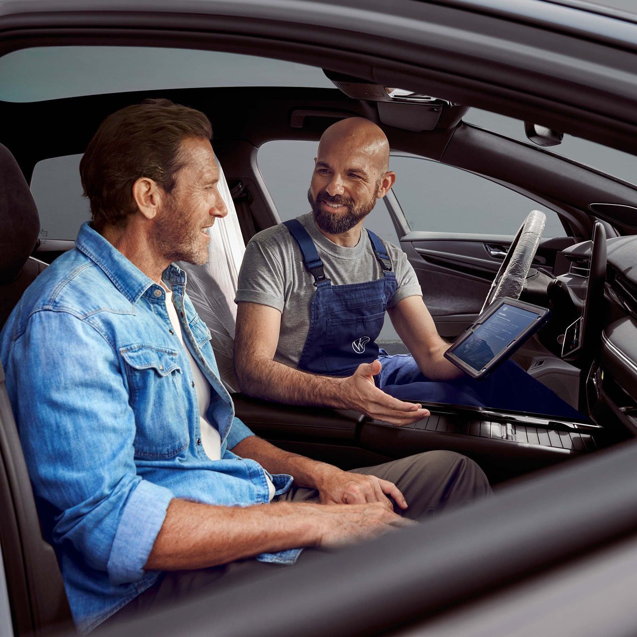 Kunde sitzt im Auto, VW Servicemitarbeiter erklärt ihm etwas auf dem Tablet