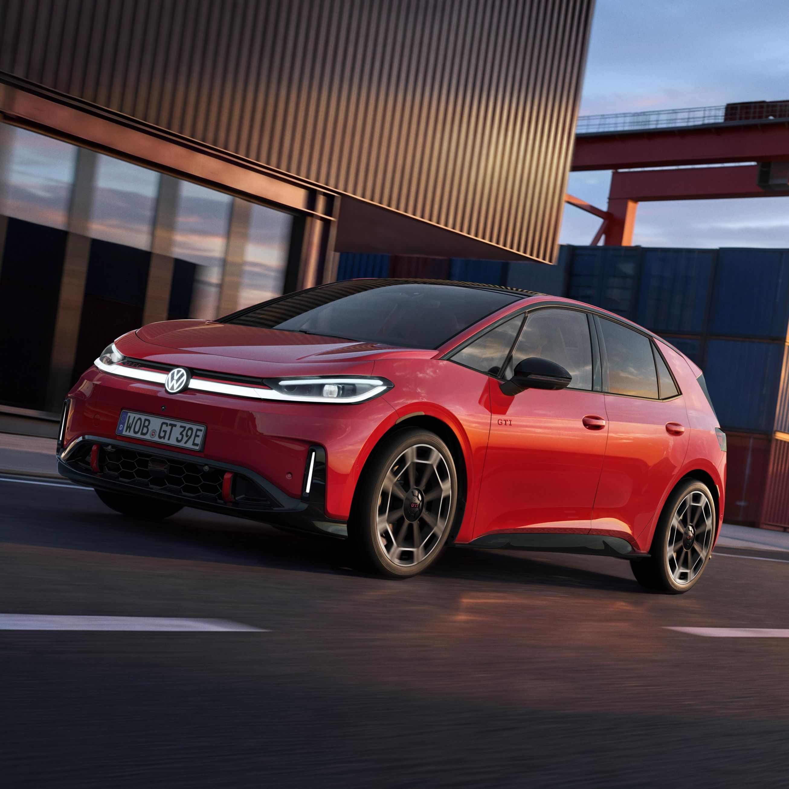 [AI-modified] – Červený VW ID.3 GTI projíždí kolem přístavní budovy se zapnutými světlomety a rozsvíceným logem.