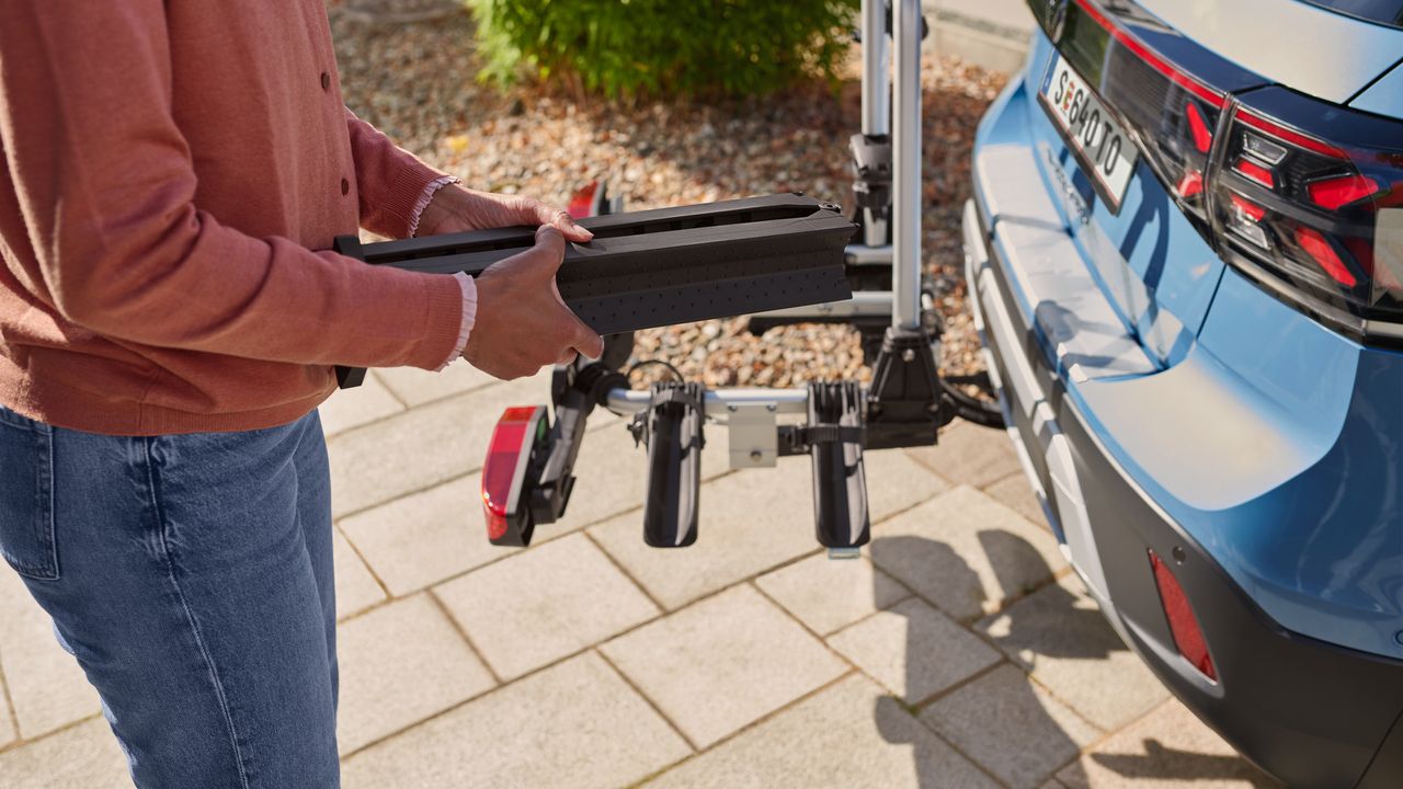 Eine Frau montiert eine Auffahrschiene am Heck eines blauen Volkswagen T-Cross