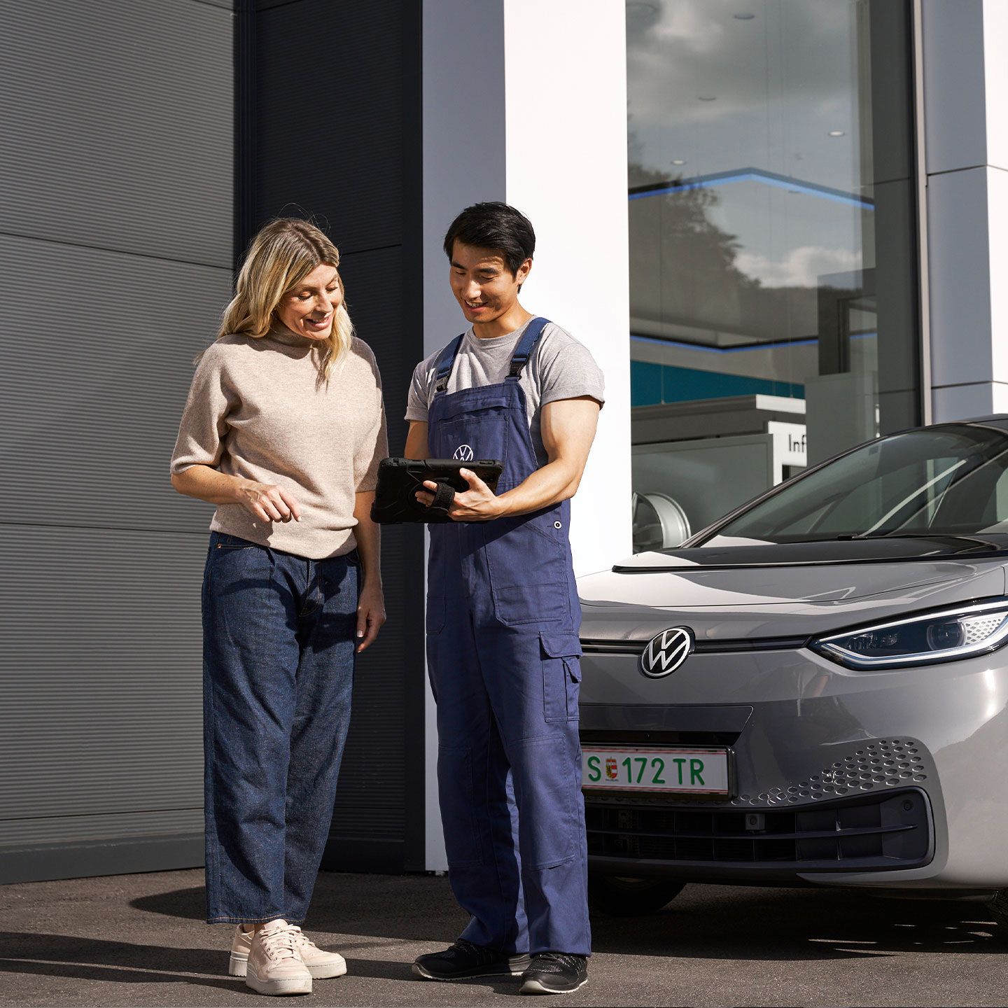 Ein Volkswagen Techniker und eine Kundin stehen vor einem grauen Volkswagen ID.3