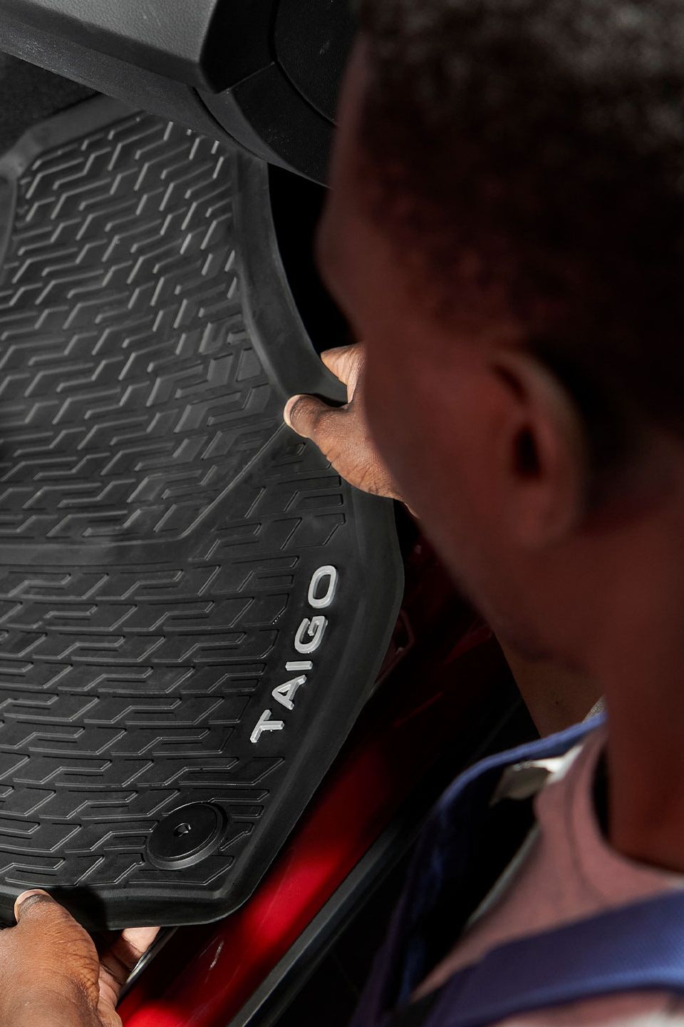 Ein Volkswagen Mitarbeiter legt eine Gummifußmatte mit Taigo Schriftzug in einen Volkswagen.