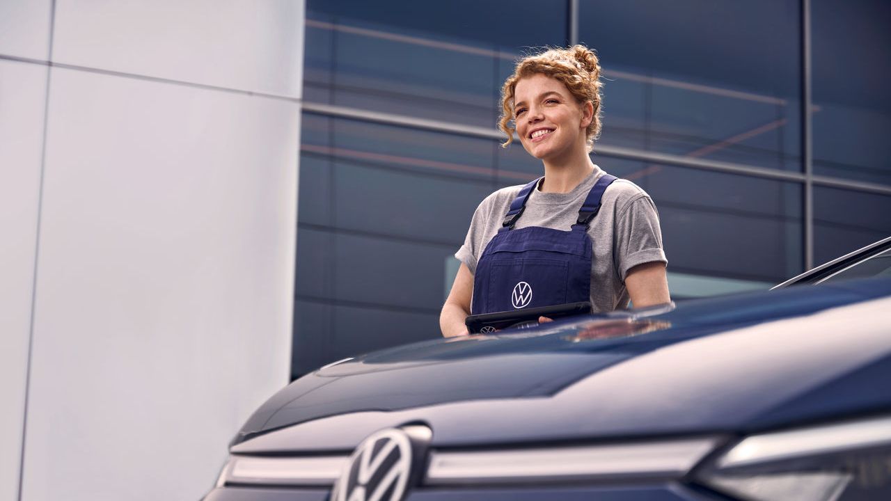 Eine Volkswagen Technikerin vor einer Volkswagen Werkstatt.