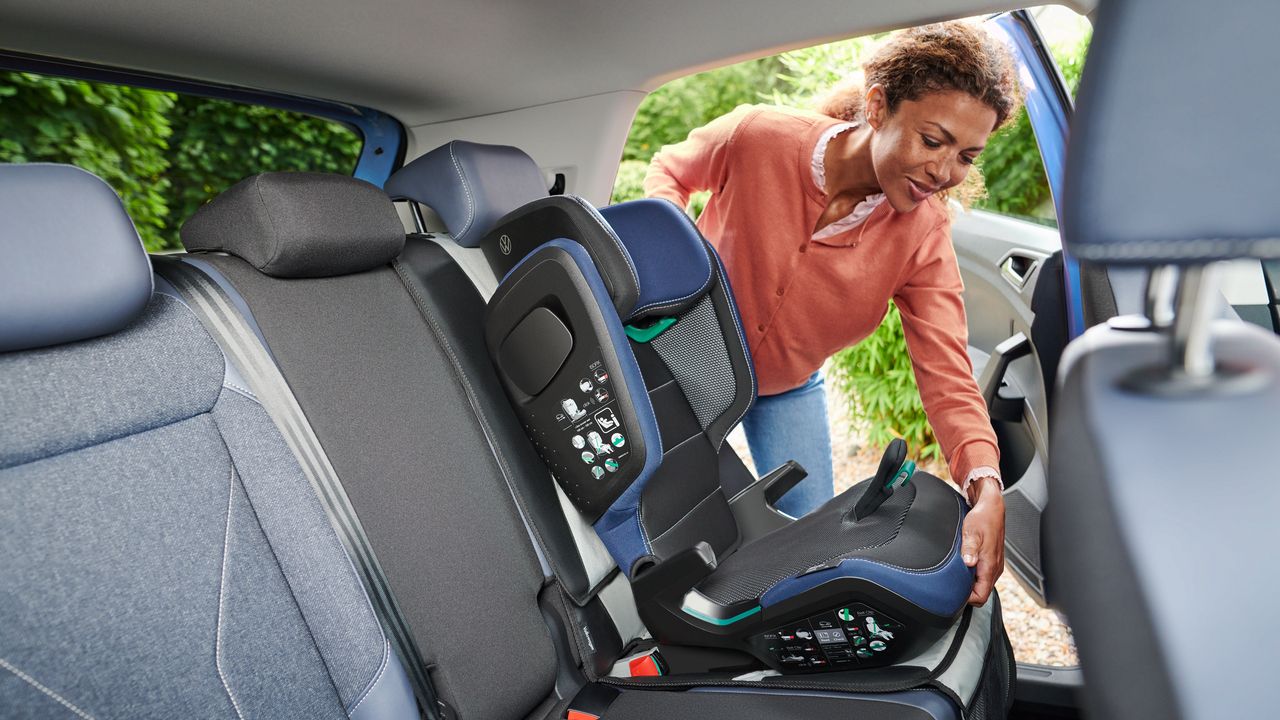 Eine Frau montiert einen Volkswagen Original i-Size KIDFIX Kindersitz in Fahrtrichtung auf der Rückbank eines Volkswagen.