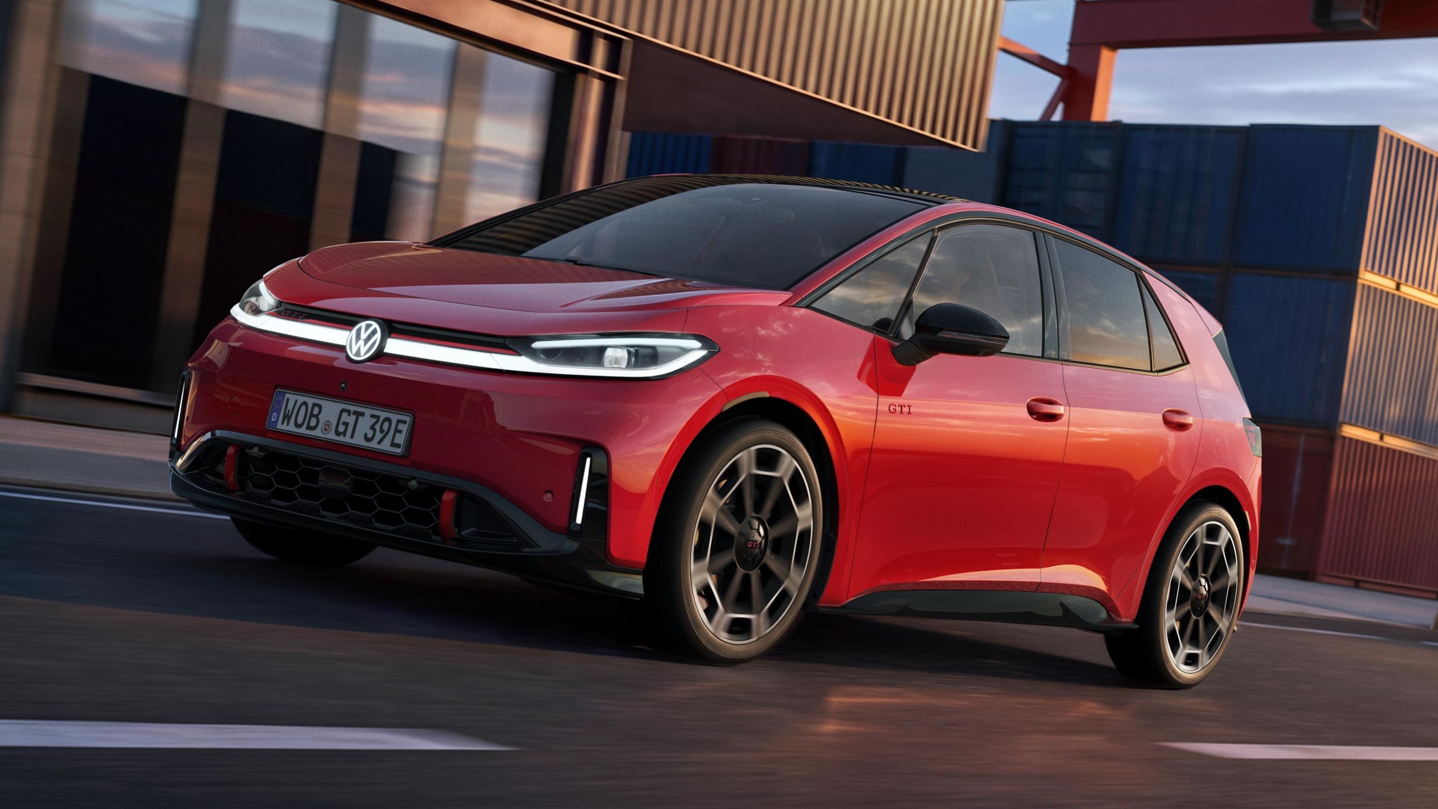 [AI-modified] – Červený VW ID.3 GTI projíždí kolem přístavní budovy se zapnutými světlomety a rozsvíceným logem.