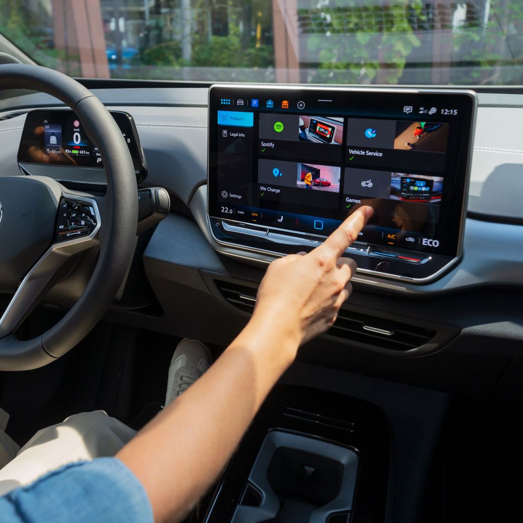 Ansicht vom Interior des ID.4 Pro mit Person welche eine Hand am Lenkrad und die andere am Infotainmentsystem hat.