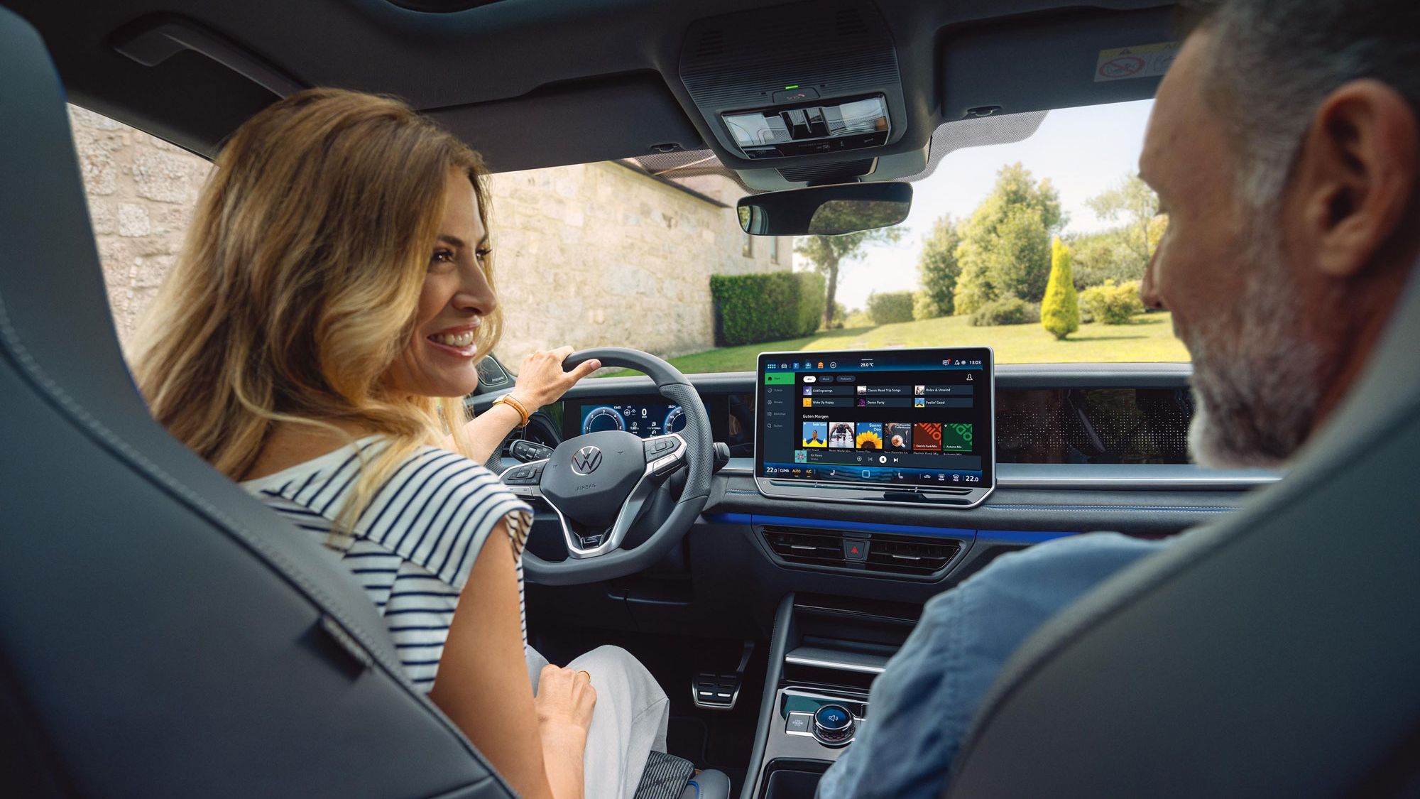 Řidič a spolujezdec ve voze Volkswagen; pohled na digitální kokpit a centrální displej systému infotainmentu.