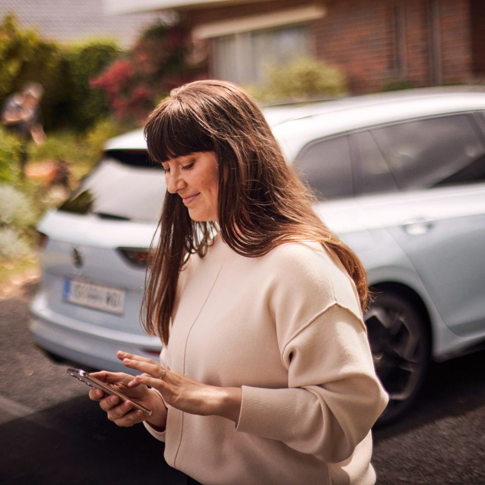  Eine Frau blickt außerhalb ihres weißen VW Golf Variant auf ihr Smartphone.