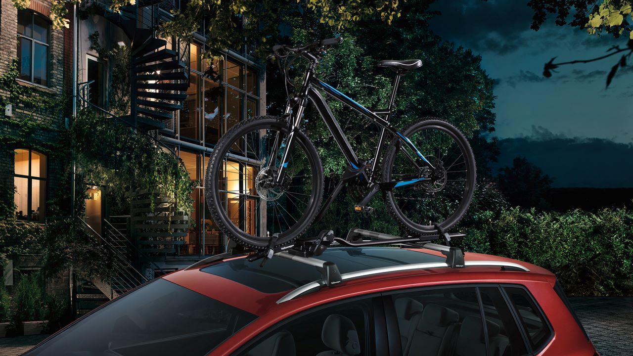 Ein roter Golf Sportsvan mit Fahrrad auf dem Dach, das auf einem Fahrraddachträger befestigt ist.