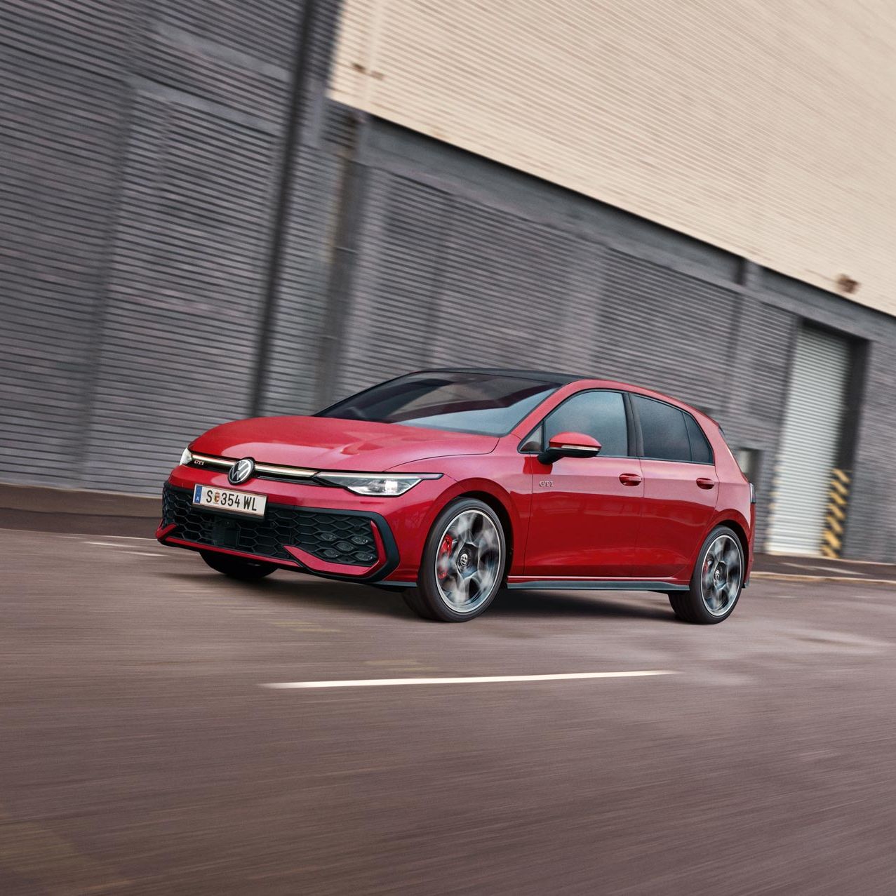 Ein roter VW Golf GTI fährt vor einer Lagerhalle entlang.