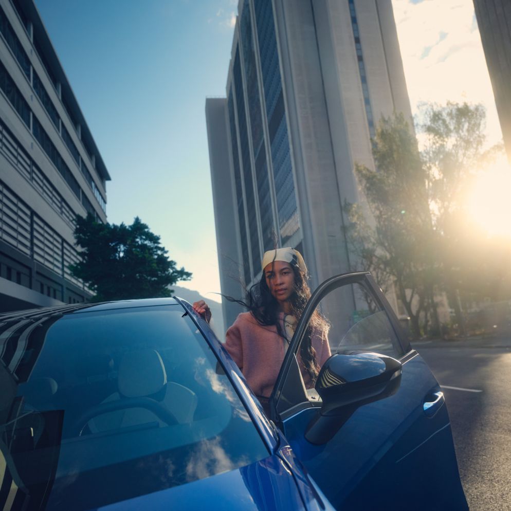 Ein blauer VW ID. Polo Style parkt in einer Stadt im Sonnenuntergang, eine Frau steigt auf der Fahrerseite aus.