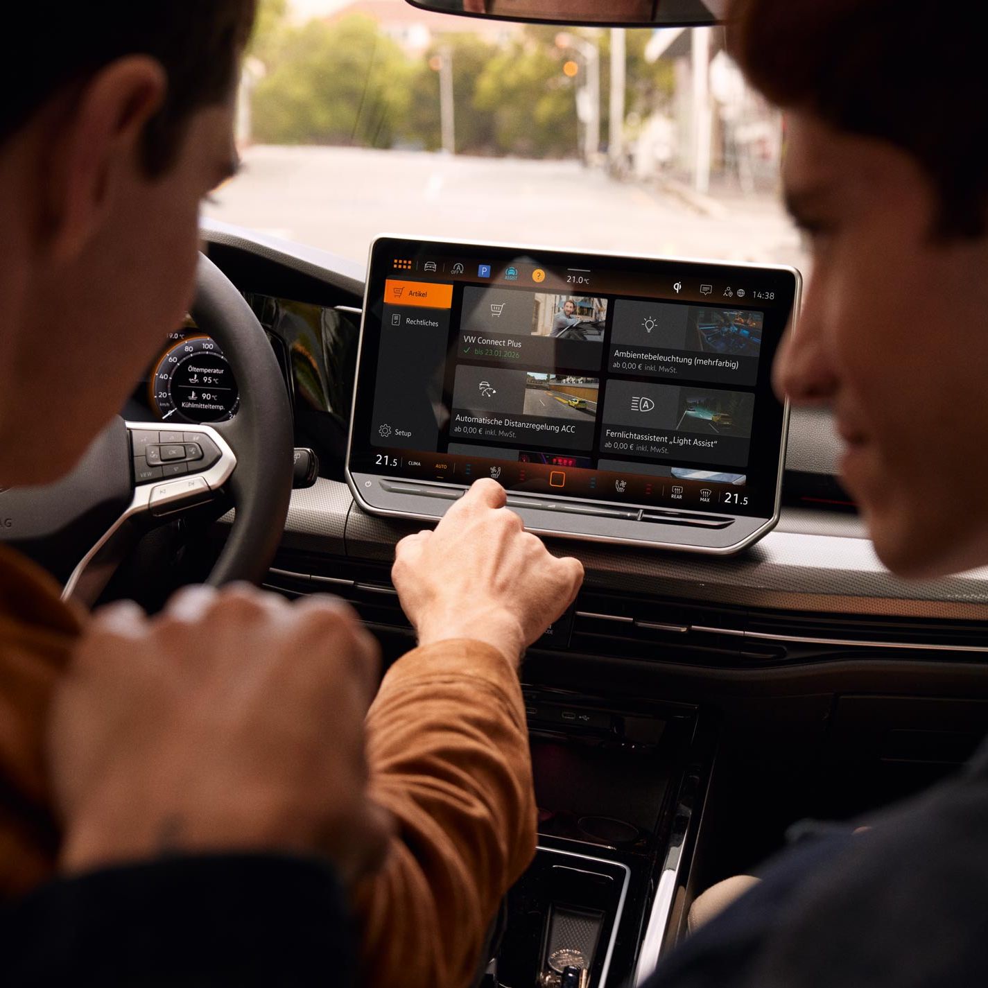 Innenansicht des VW Golf mit Blick auf das Display. Männer auf Fahrersitz und Beifahrersitz bedienen das Infotainment-System.