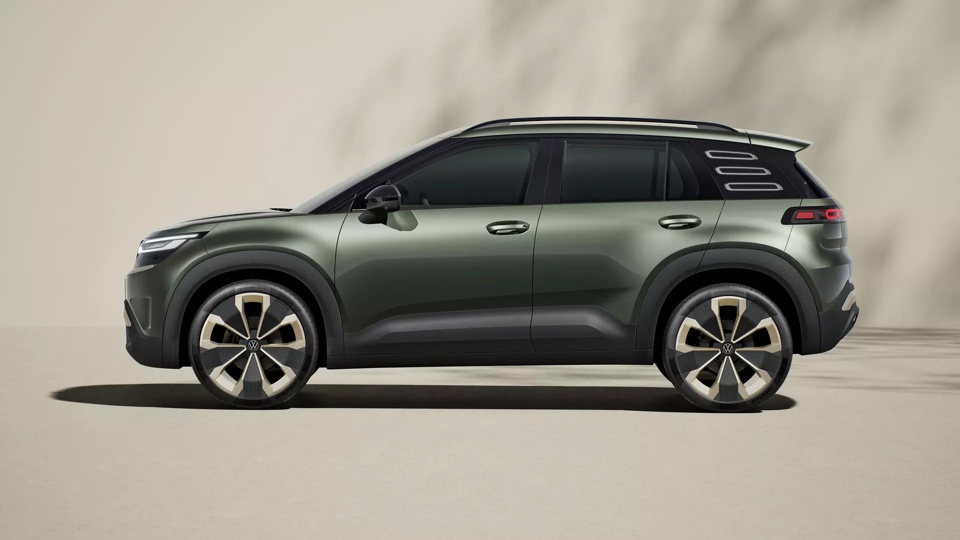 Ein modernes SUV in dunklem Grün steht vor einem neutralen Hintergrund. Das Fahrzeug hat große Felgen und eine markante Silhouette. Schattenmuster sind auf dem Hintergrund zu erkennen.