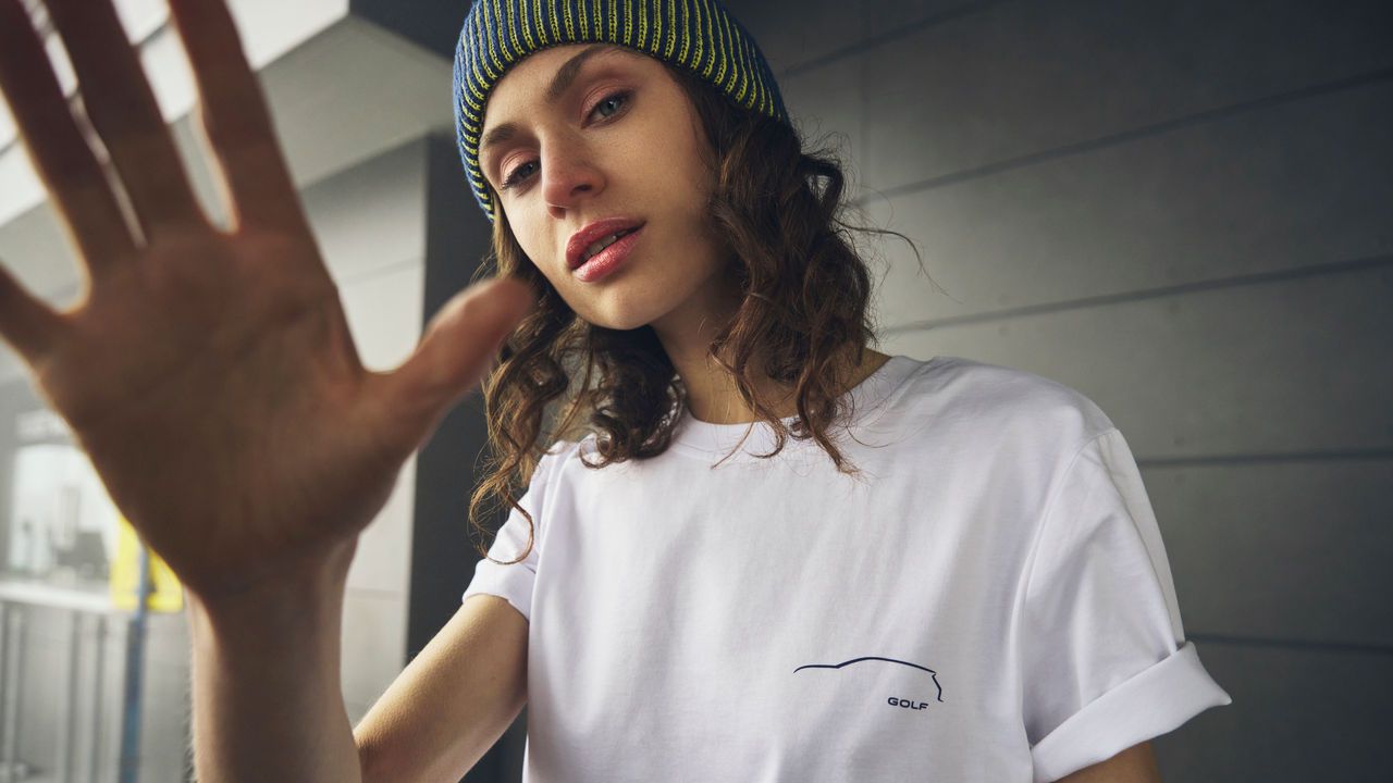 Eine junge Frau mit einem weißen T-Shirt mit aufgedrucktem Golf Logo.