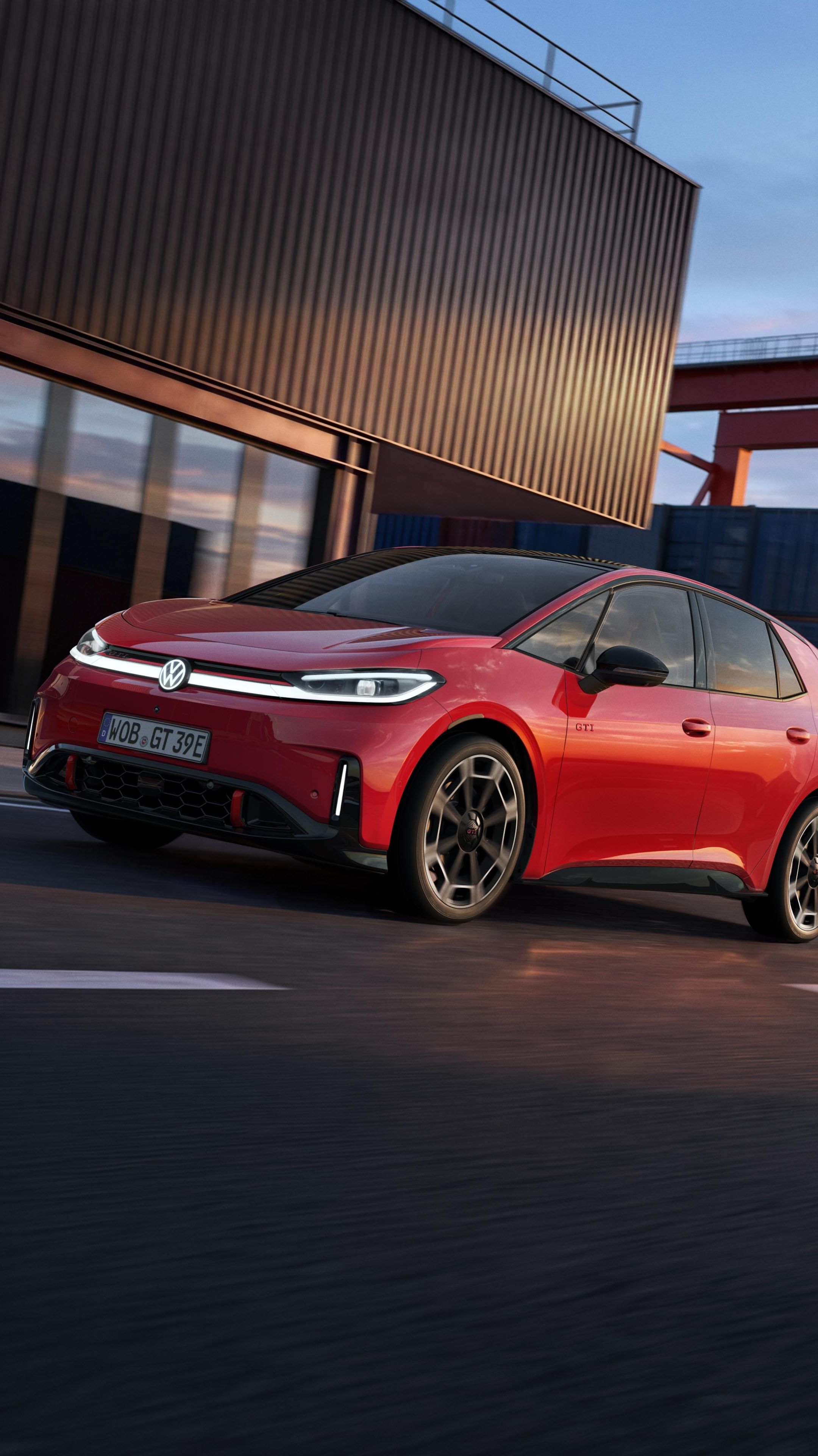 [AI-modified] – Červený VW ID.3 GTI projíždí kolem přístavní budovy se zapnutými světlomety a rozsvíceným logem.